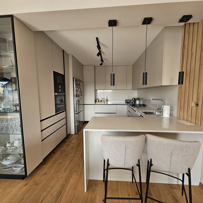 Elegantna kuhinja s modernim dizajnom, istaknuta staklenim elementom koji unosi profinjenost i lakoću u prostor. S desne strane, dekorativne drvene letvice koje dodaju toplinu i sofisticiran vizualni kontrast.